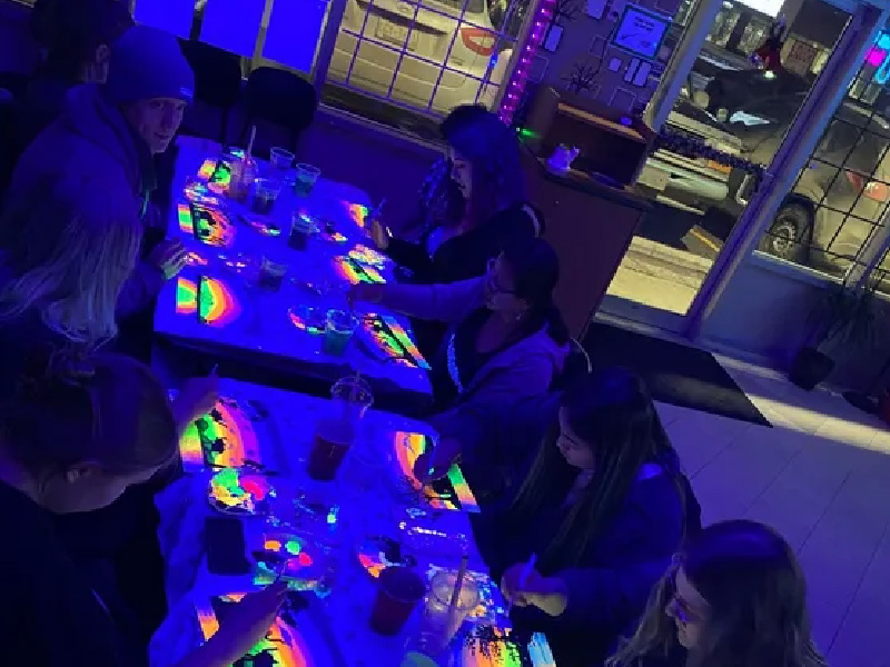 Group of people sitting at a table painting in neon colours