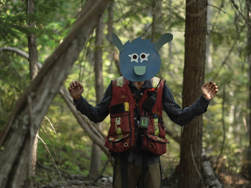 A person standing in the woods with a mask holding out their arms